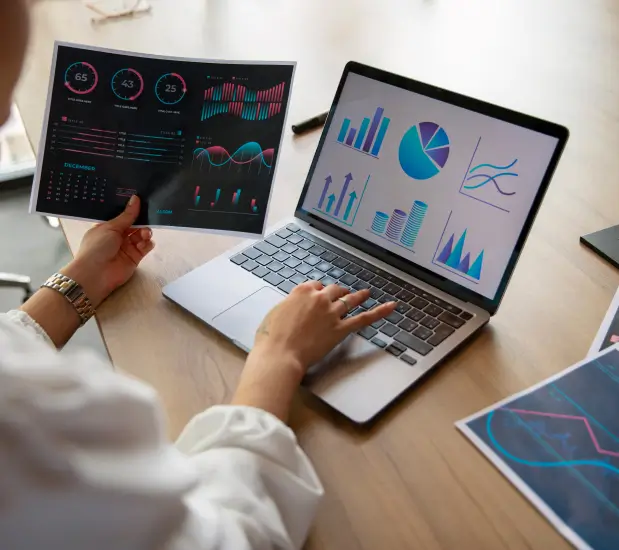 person-on-laptop-while-holding-some-graphs-printed-on-paper person on laptop while holding some graphs printed on paper